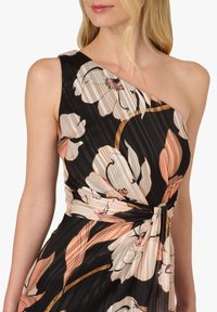 Ein einseitig schulterfreies Blumenkleid mit schwarzem Grundstoff, großen cremefarbenen und pfirsichfarbenen Blumen sowie einem geknoteten Taillendetail. Strukturierter Stoff mit dezenten Streifen.