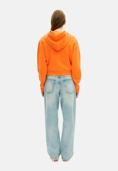 Oranje cropped hoodie met een trekkoordcapuchon en loszittende lichtblauwe jeans met een vervaagde wassing en standaard achterzakken.