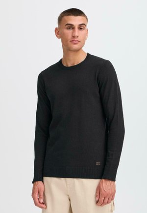 Suéter negro de cuello redondo hecho de tela suave, con mangas largas, puños y dobladillo acanalados, y un pequeño logo en la parte inferior izquierda.