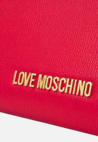 Portofel din piele roșie texturată, cu logo-ul „LOVE MOSCHINO” aurit. Finisaj neted cu un model de pori pronunțat, formă compactă și rectangulară.