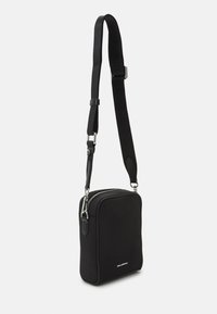 Černá obdélníková crossbody taška s nastavitelným popruhem, stříbrným zipem a malým bílým logem "KARL LAGERFELD" ve spodním středu.