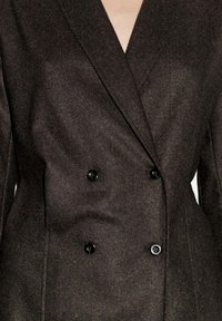 Hnědý dvouřadý blazer vyrobený z texturované látky, s velkými černými knoflíky a strukturovaným límcem.