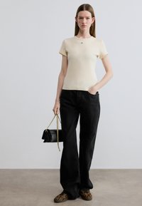 Μπλούζα σε εκρού με ριγέ υφή και κοντά μανίκια, σε συνδυασμό με ψηλόμεσα μαύρα φαρδιά τζιν παντελόνια. Συμπληρωμένο με μικρή μαύρη τσάντα και παπούτσια με λεοπάρ σχέδιο.