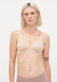Beige bra with scalloped edges, smooth fabric, and molded cups. Wide straps for support, featuring a simple, seamless design.