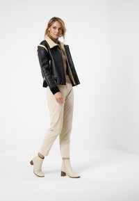 Zwarte leren jas met beige schapenvacht voering, beige coltrui, lichtbeige broek en crèmekleurige enkellaarsjes met een gestapeld hak.