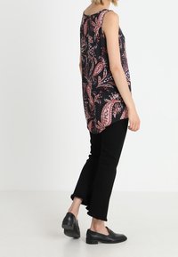 Sleeveless black tunic with red paisley pattern, paired with black cropped pants and black loafers. Smooth fabric with a flowy design.