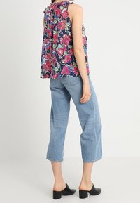 Haut sans manches à imprimé floral avec un col haut de couleur marine, orné de fleurs roses et vertes ; associé à un jean court en denim clair et des mules à talon carré noires.