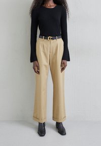 Haut noir côtelé à manches longues associé à un pantalon beige taille haute avec un ourlet retroussé et une ceinture noire à boucle dorée. Bottines noires.