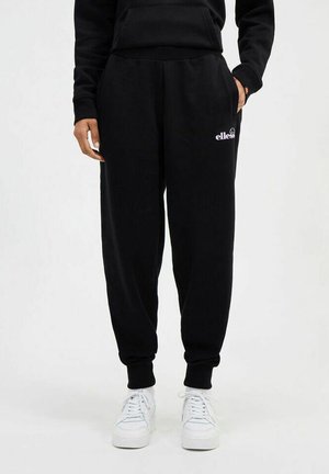 Zwarte sweatpants met elastische tailleband en manchetten, met een wit logo op het linkerpand. Gecombineerd met witte sneakers.