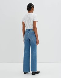 Wide-leg blue denim jeans with a high waist, subtle fading, and back pockets, paired with a white short-sleeve t-shirt and black flats.