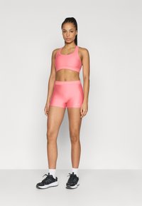 Ροζ αθλητικό σετ με κοντό τοπ και σορτς, κατασκευασμένο από λείο ύφασμα με διακριτική γυαλάδα· διαθέτει ελαστική ζώνη και λεπτομέρειες με λογότυπο.