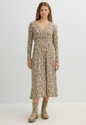 Vestido de manga larga en beige con patrones de hojas oscuros, con escote en V, cintura fruncida y longitud midi, combinado con botas de cordones en un tono beige claro.