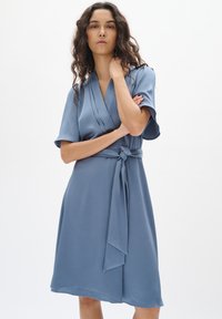 Blaues Wickelkleid aus glattem Stoff, mit kurzen Ärmeln, einer gebundenen Taille und einem knielangen Saum mit einem subtilen strukturierten Muster.
