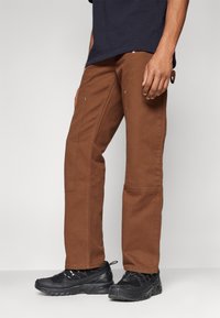 Brown cotton pants with a straight-cut design, featuring side pockets. Paired with black, textured sneakers.