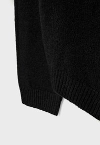 Črni pulover iz pletenine z dodatki teksture, rebrastimi manšetami in diagonalnim robom, narejen iz mehkega, udobnega materiala.