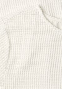 Tissu en maille gaufrée blanche avec un bord plié et des coutures fines visibles le long du détail de la couture