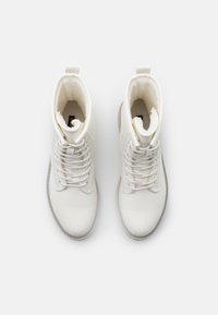 Valkoiset nahka nilkkurit, joissa on nauhakiinnitys, pyöristetty pää ja pehmeä vuori. Sateenjalka on varustettu vetotarralla kantapäässä ja harmaalla pohjalla.