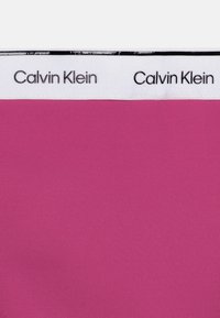 Rózsaszín Calvin Klein derékpánt sima, rugalmas anyagból készült, fekete színű, ismétlődő logós szöveggel, amely fehér háttéren található.