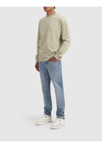 Lichtgroene sweater met een ronde hals, geribbelde manchetten en een comfortabele pasvorm, gecombineerd met lichtblauwe jeans en witte sneakers.