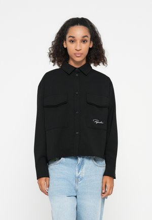 Black button-up shirt with two chest pockets and embroidered logo. Made from a smooth fabric, featuring a cropped design and pointed collar.