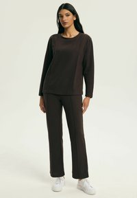 Brązowa bluzka z długim rękawem i zaokrąglonym dekoltem, zestawiona z pasującymi brązowymi spodniami. Oba elementy mają przeszywane szwy i wykonane są z miękkiego materiału.