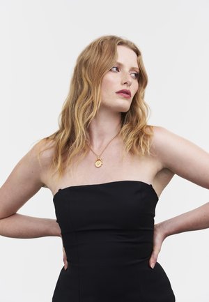 Black strapless dress with a smooth texture worn by a person. A gold necklace with a circular pendant rests on the neckline.