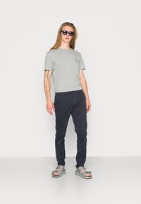 T-shirt en coton gris avec un col rond, chinos légers navy, et sandales grises, sur fond blanc.
