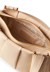 Beige Lederhandtasche mit einem strukturierten Innenraum. Sie verfügt über einen goldenen Reißverschluss und ein rechteckiges Patch, das mit dem Markennamen geprägt ist.