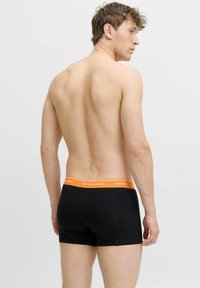 Melnas boksa bikses ar oranžu jostas daļu, uz kuras ir "JACK & JONES" zīmols. Audums izskatās gluds, ar cieši pieguļošu dizainu.