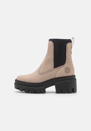 Stivali alla caviglia beige con pannello elastico nero laterale, suola in gomma nera chunky e dettagli prominenti del logo sul tallone. Finitura in suede liscia.