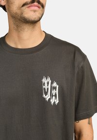 Donkergrijze katoenen t-shirt met een ronde halslijn en korte mouwen. Heeft een witte grafische afbeelding op de linkerborst met gestileerde letters "UA."