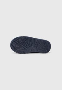Suela de zapato de goma de color azul oscuro con un patrón de relieve texturizado y el logo de UGG. Presenta ranuras angulares y crestas elevadas para mayor tracción.