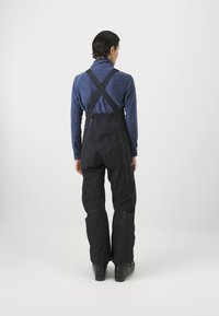 Schwarze wasserdichte Latzhose mit verstellbaren Schulterträgern, ausgestattet mit einer glatten Textur und Reißverschlusstaschen an den Seiten.