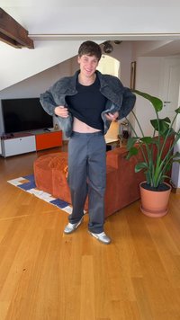 Mees, kes kannab musta t-särki, halli pükse ja teksariietust, tõstab teksajopet, seistes puidust põranda peal poti taime lähedal.