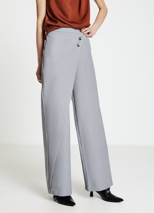 Pantaloni ampi grigio chiaro con una texture liscia, chiusura con doppio bottone in vita e cuciture laterali inclinate, abbinati a tacchi neri.