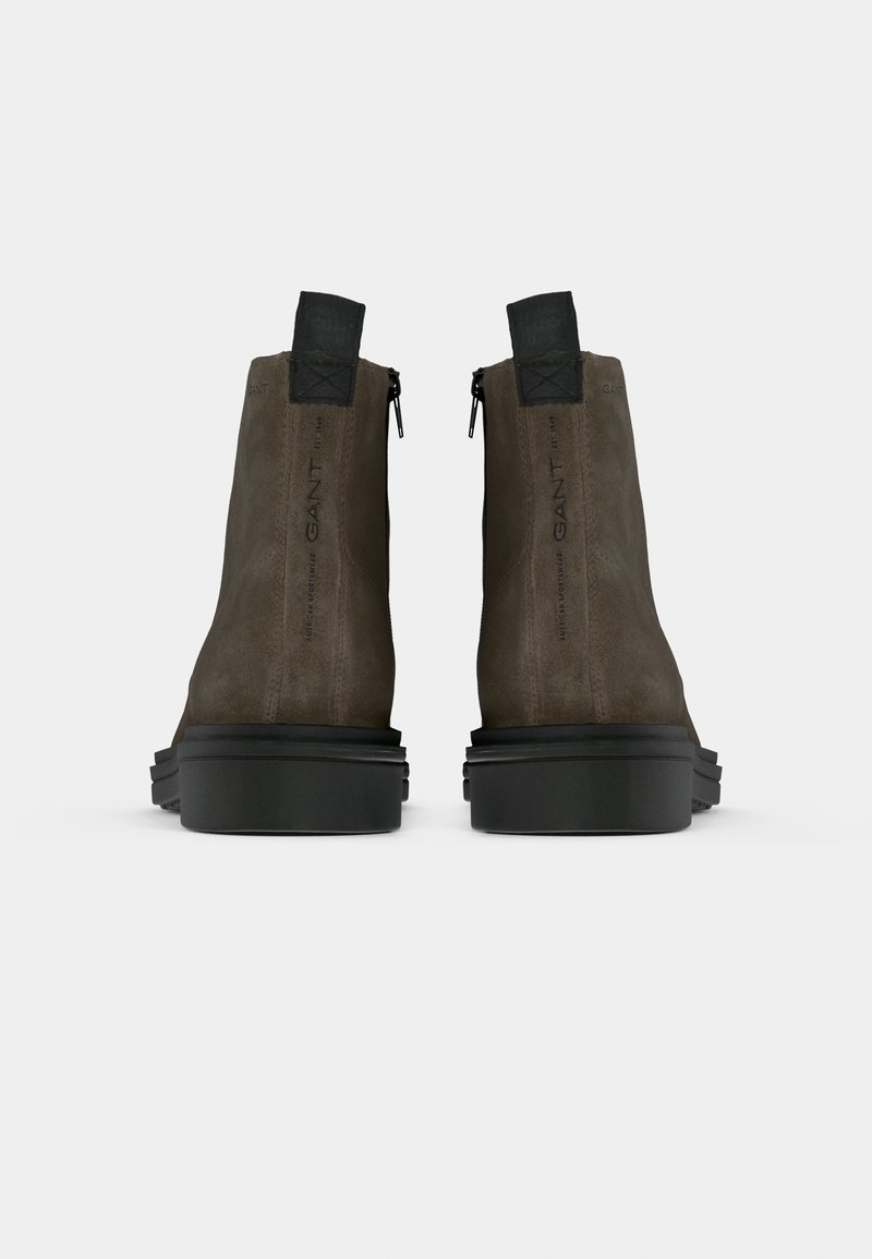 Botas de tobillo de ante marrón con un diseño elegante, cierre de cremallera, tiradores traseros prominentes y suelas de goma negra resistentes.