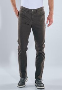 Braune Baumwollmischungshose mit einer taillierten Passform, fünf Taschen und Knopfverschluss, kombiniert mit grauen Sneakers mit weißen Akzenten.