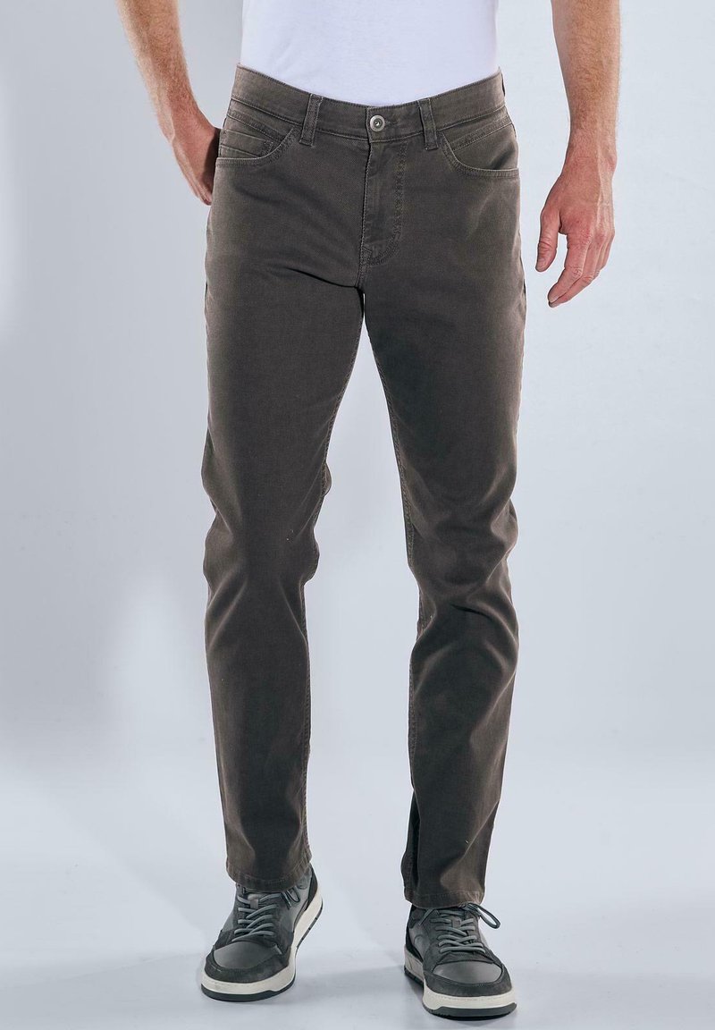 Braune Baumwollmischungshose mit einer taillierten Passform, fünf Taschen und Knopfverschluss, kombiniert mit grauen Sneakers mit weißen Akzenten.