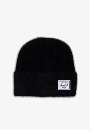 Zwarte gebreide beanie met een zachte, fluweelachtige textuur, met een omgeslagen boord en een wit rechthoekig label met zwarte tekst aan één kant.