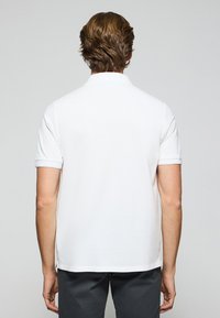 Polo shirt bianco in cotone con maniche corte, colletto e spacchi laterali. Design pulito con una texture liscia, senza motivi o accenti visibili.