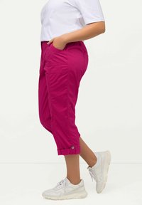 Pantalons courts roses avec une coupe décontractée, présentant des poches latérales et des ourlets retroussés. Portés avec des baskets blanches, mettant en avant un style décontracté.