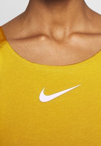Gul ärmlös topp i mjukt tyg, med en vit Nike swoosh-logotyp på bröstet och en slät, strukturerad halsringning.