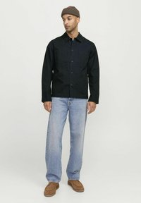 Zwarte spijkerstof spijkerjack met knoopsluiting, twee borstzakken, gecombineerd met lichtblauwe rechte jeans en bruine instapschoenen. Bruine beanie.