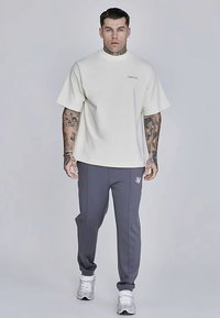 Witte T-shirt met korte mouwen, een ronde hals en een logo, gecombineerd met grijze taps toelopende joggingbroek met zijstrepen en een klein embleem.