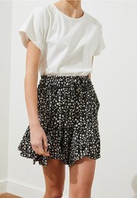 Top blanco de manga corta combinado con una falda negra floral que cuenta con un dobladillo con volante y cintura elástica. La falda tiene pequeñas flores blancas y rosas.