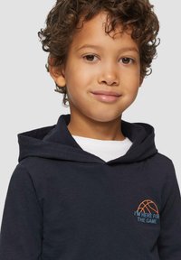 Marineblauwe hoodie met een kangoeroezak, voorzien van een oranje basketbalafbeelding en de tekst "IK BEN HIER VOOR DE WEDSTRIJD," zacht materiaal en een ontspannen pasvorm.