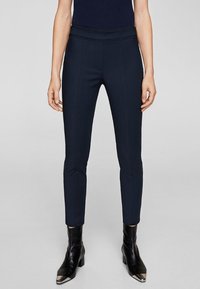 Marineblauwe broek met een aansluitend ontwerp, een gladde textuur en een hoge taille. Gecombineerd met zwarte enkellaarsjes met metallic neuzen.