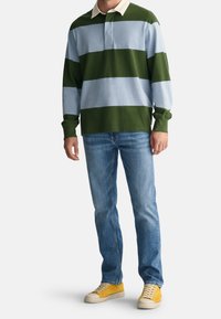 Groen- en lichtblauw gestreept rugbyshirt met een crèmekleurige kraag, gecombineerd met een blauwe spijkerbroek en gele sneakers. Casual, ontspannen pasvorm.