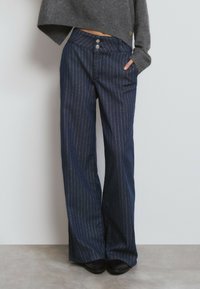 Pantalones de mezclilla a rayas navy con cintura alta, que cuentan con dos botones, bolsillos laterales y un corte de pernera ancha. Textura suave.