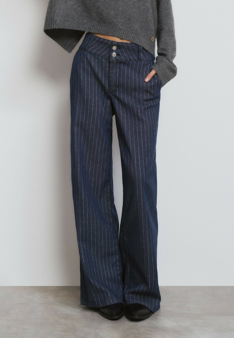 Pantalones de mezclilla a rayas navy con cintura alta, que cuentan con dos botones, bolsillos laterales y un corte de pernera ancha. Textura suave.